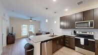 This well-appointed one-bedroom, one-bathroom apartment at Cool Springs Drive in Elizabethtown, Kentucky offers a thoughtfully designed single-floor layout. The open-concept living and kitchen area serves as the heart of the home, where rich dark-wood cabinetry, granite countertops, and a full suite of stainless steel appliances—including a refrigerator, range, microwave, and dishwasher—create a modern, functional kitchen. A peninsula with seating provides a casual dining option, accented by stylish pendant lighting overhead. The living room features crown molding, a ceiling fan, and light hardwood-style flooring, with a glass door opening to outdoor access and allowing natural light to fill the space. The bedroom is a comfortable retreat with plush carpeting, a ceiling fan, and a large window framing outdoor views. Multiple closets, including a dedicated laundry space and hallway storage, offer generous organization options throughout. The bathroom is clean and neutral, featuring a granite-topped vanity with dark cabinetry, a full tub-shower combination, and wood-style flooring. Recessed lighting and a consistent neutral color palette throughout give the entire apartment a bright, cohesive feel.
