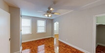 This single-floor studio is thoughtfully laid out to maximize its compact footprint. The main living area is an immediate standout, showcasing beautifully polished parquet wood flooring in a rich warm tone that extends throughout the space. Neutral gray walls, crisp white baseboards, and a ceiling fan with integrated lighting contribute to a clean, functional ambiance. Natural light filters in through double windows dressed with white blinds, lending the room an airy feel. Two closets flank the entry door, offering generous storage for a studio of this scale.

An elegant arched doorway connects the living area to the kitchen, which features light wood cabinetry, dark countertops, and tile flooring. The kitchen is equipped with a gas range, refrigerator, and a single-basin sink, providing all essential cooking amenities within an efficient galley-style layout. The bathroom is accessible from the main living space and includes a full bathtub with shower, white tile surround, and a wall-mounted sink. The overall design is straightforward and practical, making this studio a well-organized, move-in-ready space with classic details throughout.
