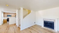 This two-story home offers a well-organized layout with three bedrooms and three full bathrooms spread across two equally proportioned floors. The main level features a bright, open living room with light hardwood-style flooring, a textured ceiling, and a sliding glass door flanked by vertical blinds that opens to the outdoors, filling the space with natural light. A wood-burning fireplace adds warmth to the living area, which flows toward a staircase connecting to the upper floor. The kitchen is well-appointed with warm maple cabinetry, white quartz countertops, stainless steel appliances including a range, microwave, and refrigerator, plus a skylight overhead and a peninsula for additional workspace. Conveniently adjacent is a dedicated laundry room with side-by-side washer and dryer units. The bathrooms are clean and functional, featuring warm wood vanities, white quartz countertops, undermount sinks with chrome fixtures, and full tub-shower combos with natural light from blinds-fitted windows. Bedrooms on the upper floor are carpeted and bright, with large windows overlooking the surrounding neighborhood and generous double-door closets providing ample storage. Throughout the home, a neutral color palette and consistent hardwood-style flooring on the lower level create a cohesive, move-in-ready aesthetic.