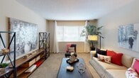 This single-floor residence offers a thoughtfully arranged layout that balances comfort and functionality across its key living spaces. The living room features neutral-toned carpet, a textured ceiling, and a large window dressed with white curtains and blinds, allowing generous natural light to fill the room and create an inviting atmosphere.

Adjacent to the living room, the dining area is anchored by a sliding glass door fitted with vertical blinds and curtain panels, providing outdoor views and additional natural light. The space comfortably accommodates a dining table and chairs, making it suitable for everyday meals and entertaining.

The galley-style kitchen is lined with warm wood cabinetry on both sides, offering ample storage. White appliances, including a range and refrigerator, complement the neutral countertops, while tile flooring runs underfoot.

The primary bedroom is carpeted and features large windows with outdoor greenery views, while a second bedroom offers similar proportions and natural light. Both rooms provide a calm, restful environment.

Two full bathrooms serve the residence, each featuring tile flooring, a vanity with wood cabinetry, granite-style countertops, and a shower-tub combination with a curtain. The overall palette throughout the home is warm and neutral, contributing to a cohesive and comfortable living environment.