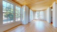 This well-crafted three-floor home showcases a cohesive design language anchored by natural wood plank ceilings and light hardwood floors throughout the main living areas. The open living space is defined by an abundance of natural light streaming through large multi-pane windows, complemented by sheer drapery that softens the bright, airy atmosphere and frames views of mature surrounding trees.

The kitchen is a standout feature, equipped with premium stainless steel appliances including a professional-grade range and French door refrigerator. A generous marble-topped island anchors the space, while white shaker cabinetry, a subway tile backsplash, and a statement pendant light complete the refined yet functional design.

The bathrooms are finished with careful attention to detail. One features hexagonal blush floor tiles, a marble-topped vanity, and a glass-enclosed walk-in shower with white subway tile and brushed gold fixtures. A second bathroom offers a clean white palette with matte black hardware and hexagonal tile flooring.

Upper-floor bedrooms are carpeted for comfort and receive ample natural light through multi-pane windows. The stairwells are well-lit with contemporary wall sconces. The attached garage features an automatic opener, exposed wood beam ceiling, and a polished concrete floor, providing practical and spacious vehicle storage.