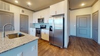This single-floor residence offers a thoughtfully designed open-concept layout that seamlessly connects the kitchen and living area. The kitchen is a standout feature, equipped with stainless steel appliances including a side-by-side refrigerator, electric range, and built-in microwave. White shaker-style cabinetry reaches to the ceiling, complemented by a light blue subway tile backsplash and a generous granite-topped island with an undermount sink and pendant lighting above. Rich dark hardwood-style flooring runs throughout the main living areas, while large windows with blinds invite abundant natural light and outdoor views. The living area is enhanced by a ceiling fan and crown molding details.

The bedrooms are carpeted and well-sized, each featuring ceiling fans, crown molding, and windows with natural light. The primary bedroom includes access to a walk-in closet. Two bathrooms mirror each other in design, each showcasing dual undermount sinks set in granite countertops, white cabinetry with brushed nickel hardware, large framed mirrors, and tiled walk-in showers. Throughout the space, consistent finishes — including dark baseboards, crown molding, and neutral wall tones — contribute to a cohesive and modern aesthetic.