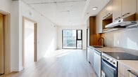 Located in the heart of Ottawa's downtown core at 75 Slater Street, this thoughtfully designed one-bedroom, one-bathroom unit offers a compact yet efficient layout with contemporary finishes throughout. The open-concept living area is anchored by light-toned hardwood flooring and exposed concrete ceilings, lending an industrial-modern character to the space. Large floor-to-ceiling windows flood the living area with natural light and frame impressive views of the Ottawa skyline, creating a bright and airy atmosphere. The kitchen is efficiently designed with two-tone cabinetry featuring warm wood-grain lower cabinets and taupe upper cabinets, a marble-inspired tile backsplash, quartz countertops, stainless steel appliances including a dishwasher and electric range, and a black matte faucet over an undermount sink. The bedroom benefits from its own floor-to-ceiling window offering sweeping city views and generous natural light. The bathroom is a standout space, featuring dramatic dark hexagonal tile flooring, a floating walnut vanity with a black countertop and matte black fixtures, and a marble-tiled tub-shower combination. A dedicated entrance and hallway complete this well-appointed urban unit.