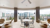 Located at 131 Poindexter Drive in Charlotte's vibrant South End neighborhood, this contemporary single-floor space offers a refined and open living environment with a clean, modern aesthetic. The living room is the heart of the space, characterized by crisp white walls, smooth light-toned flooring, and a sleek linear fireplace set into a full wall of floor-to-ceiling built-in cabinetry — a striking architectural focal point that adds both function and elegance. A wall-mounted flat-screen television complements the media wall, while woven rattan-style lounge chairs and a patterned area rug introduce warmth and texture against the minimalist backdrop. Large floor-to-ceiling glass doors with dark-framed paneling flood the interior with abundant natural light and create a seamless visual connection between the living room and the balcony. The balcony extends the living space outdoors, offering expansive elevated views of Charlotte's dynamic urban streetscape, including light rail activity, tree-lined intersections, and the surrounding cityscape. The overall ambiance is sophisticated yet relaxed — a balance of contemporary design and comfortable livability in the heart of one of Charlotte's most walkable and thriving urban districts.