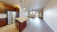 Located in Kapolei on the sunny west side of Oahu, this well-appointed one-bedroom, one-bathroom unit offers a thoughtfully designed layout with modern finishes throughout. The open-concept living and kitchen area forms the heart of the home, where rich dark wood cabinetry, granite countertops, a tile backsplash, and stainless steel appliances create a polished culinary space. A central kitchen island provides additional prep space and connects seamlessly to the living area, which features wood-style flooring, a ceiling fan, and multiple windows that fill the room with natural light. A sliding door leads to a private balcony with views of the surrounding neighborhood and gentle Hawaiian hills beyond. The bedroom is a comfortable retreat, brightened by large windows framing scenic outdoor views, also finished with wood-style flooring and a ceiling fan. A walk-in closet with built-in wire shelving offers generous storage. The bathroom is finished with dark tile flooring, a granite-topped vanity with wood cabinetry, and a full soaking tub with tiled surround. Clean white walls and consistent flooring throughout give the space a cohesive, move-in-ready feel ideal for comfortable island living.