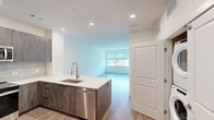 Located at 2800 Brighton Blvd in Denver's RiNo neighborhood, this modern one-bedroom, one-bathroom unit offers a thoughtfully designed open-concept layout. Light wood-tone flooring flows throughout the space, complementing the clean, neutral color palette that enhances the bright, airy ambiance.

The kitchen is a standout feature, equipped with stainless steel appliances including a refrigerator with ice maker, electric range, built-in microwave, and dishwasher. Dark wood-grain cabinetry extends to the ceiling, paired with a sleek tile backsplash and white quartz countertops. A kitchen island with an undermount sink and a brushed nickel pull-down faucet serves as a natural divider between the kitchen and the open living area, which receives ample natural light through large windows.

The spacious bedroom includes a ceiling fan and connects to a generously sized walk-in closet outfitted with adjustable shelving and double hanging rods on multiple walls, offering excellent storage capacity.

The bathroom is elegantly appointed with large-format marble-look tile flooring, a wide dual-sink vanity with quartz countertops, dark cabinetry, and a well-lit mirror. An in-unit washer and dryer are also included. The overall design emphasizes modern finishes and functional living in one of Denver's most dynamic neighborhoods.