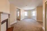 This single-floor unit showcases a thoughtful layout with a variety of architectural details that give the space a distinctive character. The main living area is expansive, featuring warm beige carpeting, a textured ceiling, and a classic white-mantled decorative fireplace with a tile surround, adding a refined focal point to the room. A standout architectural feature is the curved bay area at the far end of the living space, lined with multiple windows that invite ample natural light and create an open, airy atmosphere. This rounded alcove transitions seamlessly from carpet to hardwood flooring, highlighting the design's attention to detail. A bedroom features an exposed red brick accent wall paired with a large window, lending the room an industrial-chic quality that contrasts warmly with the neutral surroundings. An adjacent bathroom is conveniently accessible from this room. The kitchen is efficiently designed with warm wood cabinetry, light countertops, a tiled backsplash, hardwood flooring, and black appliances including a range and refrigerator, along with a dishwasher. A closet near the entry provides additional storage. Overall, the space combines classic architectural elements with functional living areas.