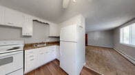 Located at 54 Whitehouse Dr in Rochester, NY, this 2-bedroom, 1-bathroom unit offers a practical and well-organized single-floor layout. The combined kitchen and living area serves as the heart of the home, with the kitchen featuring white cabinetry, dark laminate countertops, a double sink, white appliances including a refrigerator and electric range, and durable hardwood-style flooring. A ceiling fan overhead adds comfort to the space. The living room flows naturally from the kitchen, offering plush carpeting, multiple windows that invite abundant natural light, and a wall-mounted air conditioning unit for seasonal comfort. Baseboard heating runs throughout the unit, ensuring consistent warmth. Both bedrooms are carpeted and finished in neutral gray tones, each featuring windows with blinds that offer outdoor views and natural light. The primary bedroom includes a double louvered-door closet, providing generous storage. A hallway connects the bedrooms to the full bathroom, which is appointed with tile-surround tub and shower, a window for ventilation, and grab bars for added convenience. The clean, understated aesthetic and functional layout make this a practical and comfortable living space.