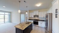 This single-story home presents a thoughtfully designed layout with a cohesive blend of modern finishes and functional living spaces. The kitchen serves as a central highlight, featuring tall white raised-panel cabinetry with matte black hardware, dark granite countertops along the perimeter, and a contrasting navy island topped with a striking variegated granite surface and an undermount sink. Pendant lighting accents the island, while stainless steel appliances — including a range, over-the-range microwave, and refrigerator — complete the space. Light wood-look flooring runs throughout the kitchen.

The bedrooms are finished with neutral carpet and warm, creamy wall tones. One bedroom offers an outdoor view through a wide double window overlooking open greenery. Bedroom closets feature paneled gray doors with rod storage. The primary bathroom includes an extended white vanity with ample drawer storage, a framed mirror, and a walk-in closet with built-in hanging rods and tile flooring. A secondary bathroom offers dark cabinetry, tile flooring, and a tub-shower combo. A dedicated laundry room accommodates a full-size washer and dryer with overhead shelving and cabinet storage.