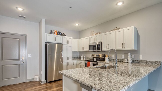 The Oval designer chef-inspired kitchen featuring granite countertops, white shaker style cabinets, granite countertops and gooseneck faucets - Ellipse Urban Apartments