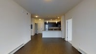 This well-appointed single-floor residence offers a clean, modern aesthetic defined by an open-concept layout that seamlessly connects the living area to the kitchen. Rich, dark hardwood flooring extends throughout the space, providing a warm and cohesive foundation that complements the contemporary design.

The kitchen serves as a central focal point, featuring dark espresso cabinetry paired with granite countertops and a peninsula that doubles as a breakfast bar. Pendant lighting hangs above the peninsula, adding both style and functional illumination. Stainless steel appliances, including a refrigerator and microwave, complete the kitchen's modern look. A mosaic tile backsplash adds a subtle decorative touch behind the sink area.

The open living area is bright and airy, with white walls and smooth ceilings that enhance the sense of space. Recessed lighting and flush-mount fixtures provide ample illumination throughout. Baseboard heating runs along the perimeter, ensuring year-round comfort. Multiple doorways lead to additional rooms, suggesting a thoughtful and functional floor plan. The overall ambiance is clean, neutral, and move-in ready, offering a versatile canvas well-suited to a variety of interior styles.