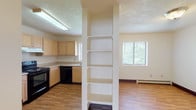 This single-floor residential unit offers a practical and functional layout designed for comfortable everyday living. The kitchen is well-equipped with light wood cabinetry, black appliances including an electric range and dishwasher, a double basin sink, and ample counter space. A window above the sink allows natural light to brighten the workspace. The kitchen opens toward the living area, which is divided by a structural column featuring built-in open shelving — a useful and distinctive architectural detail. The living area is finished with warm wood-look flooring and receives natural light through multiple windows fitted with blinds. A baseboard heating system runs throughout the unit. The spacious carpeted living room features a two-toned wall design and a window overlooking the outdoors. Bedrooms are generously sized with plush carpet flooring, baseboard heating, and natural light from windows. One bedroom includes a sliding wood-panel closet door with built-in shelving. The unit includes two full bathrooms, each with a tub and shower combination, a vanity with a single sink, mirrored medicine cabinet, and wood-look flooring. A dedicated laundry room provides washer and dryer hookups, a utility shelf, and an electrical panel, offering added convenience. Textured ceilings are present throughout the unit.