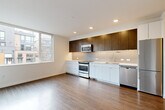 Located in Seattle's vibrant Capitol Hill neighborhood, this contemporary one-bedroom, one-bathroom apartment offers a thoughtfully designed layout with modern finishes throughout. The combined kitchen and living area forms the heart of the unit, featuring warm wood-style flooring that extends seamlessly across the entire floor. The kitchen is well-appointed with a sleek two-tone cabinetry scheme — crisp white lower cabinets paired with rich dark wood upper cabinets — complemented by a tile backsplash, white countertops, and a full suite of stainless steel appliances including a range, microwave, dishwasher, and refrigerator. Large corner windows in the living area flood the space with natural light while offering views of the surrounding neighborhood. A clean, well-lit hallway connects the living space to the private areas of the unit. The bedroom is a compact, efficient space with wood-style flooring, a sliding closet door, and a window providing additional natural light. The bathroom features a full tub and shower combo, a white vanity with ample storage, and consistent wood-style flooring. The overall aesthetic is clean, minimal, and modern, making this an efficient and well-designed urban residence.