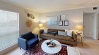 This single-floor residence offers a well-organized layout comprising a living room, galley-style kitchen, two bedrooms, and two full bathrooms. The living room features crown molding, neutral walls, and plush carpet, creating a comfortable gathering space anchored by warm lamp lighting and curated wall art. The galley kitchen is equipped with wood-toned cabinetry, laminate countertops, a double stainless steel sink, and black appliances including a range and refrigerator, all set over durable hardwood-style flooring.

The primary bedroom is generously proportioned, featuring carpet flooring, a ceiling fan with light fixture, natural light from a window with blinds, and direct access to a walk-in closet. The second bedroom offers its own distinct character, highlighted by a bold dark accent wall, carpet flooring, a ceiling fan, and a window that brings in natural light. Both bathrooms include a shower-tub combination; one features hardwood-style flooring and a wood-tone vanity with a large mirror, while the other presents a clean, all-white aesthetic with tile surround. Throughout the unit, a consistent neutral color palette and bohemian-inspired decorative touches contribute to a cohesive and inviting atmosphere.