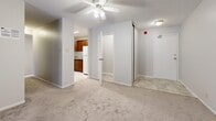 This single-floor unit offers a practical and efficient layout accommodating four bedrooms, one full bathroom, a kitchen, hallway, and closet. The open living area features neutral-toned carpet, a textured ceiling, and a ceiling fan with integrated lighting. Sliding glass doors lead to a balcony with outdoor views of the surrounding urban streetscape, allowing natural light to fill the main living space. The kitchen is equipped with warm wood cabinetry, laminate countertops, a white electric range, refrigerator, and a single-basin sink, with tile flooring tying the space together. The bedrooms are carpeted and feature neutral walls, with windows providing natural light and city views. Several bedrooms include sliding mirrored closet doors for added storage. The shared bathroom is finished with tile flooring, light-toned wall surround, and a full tub-shower combination. A central hallway connects the living areas to the bedrooms and bathroom, with a ceiling fan overhead aiding in airflow throughout. The unit's straightforward layout and consistent neutral palette provide a clean, move-in-ready foundation suitable for a variety of living arrangements.