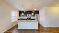 Located at 6631 Tanager Lane in Hilliard, Ohio, this single-floor home offers a thoughtfully designed layout with a clean, modern aesthetic throughout. A long entry hallway with rich hardwood-style flooring and crisp white walls leads into the main living areas, setting a welcoming tone from the moment you step inside.

The open-concept kitchen is a standout feature, showcasing floor-to-ceiling dark espresso cabinetry that provides generous storage, granite-style countertops, and a suite of stainless steel appliances including a refrigerator, range, and over-the-range microwave. A central island with a built-in sink and seating overhang serves as both a functional workspace and a casual gathering spot, illuminated by dual pendant lights overhead.

The adjoining living area is carpeted and bathed in natural light through large windows, with crown molding adding an elegant finishing touch. The seamless flow between the kitchen and living space makes the layout ideal for everyday living and entertaining alike.

The bathrooms continue the cohesive design language with dark vanity cabinetry, white countertops, and hardwood-style flooring. One bathroom features a double-sink vanity with a large mirror, while another offers a tub-shower combination. A generously sized walk-in closet with wire shelving provides ample organization space. Bedrooms are carpeted and feature neutral walls, offering a calm and versatile canvas.