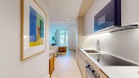 This thoughtfully designed one-bedroom, one-bathroom residence at 33 Westchester Pl in New Rochelle, NY offers a smart, efficient layout without sacrificing style or function. Light-toned hardwood flooring runs throughout, unifying the space and enhancing its bright, airy character.

The entry hallway leads directly into a sleek galley kitchen outfitted with flat-front light wood cabinetry, a white quartz countertop, stainless steel sink, induction cooktop, built-in oven, and an over-range microwave — all finished with under-cabinet lighting for a clean, modern aesthetic.

The living area features recessed lighting accented by a softly illuminated tray ceiling, creating a warm, refined ambiance. The open layout accommodates a comfortable seating arrangement alongside tasteful décor, including bold framed artwork that adds a vibrant, contemporary energy to the space.

The bedroom is a well-proportioned retreat anchored by a large floor-to-ceiling window that floods the room with natural light and frames views of the surrounding cityscape. A dedicated workspace area adds practicality to the room.

The bathroom is finished in a clean, modern style consistent with the rest of the residence. Throughout, the design emphasizes clean lines, neutral tones, and high-quality materials, resulting in a cohesive and polished living environment.