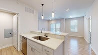 Located on Longs Peak Street in Brighton, Colorado, this well-designed 2-bedroom, 2-bathroom home offers a clean, modern aesthetic throughout its single-level layout. The open-concept kitchen and living area serves as the heart of the home, featuring a peninsula with crisp white quartz countertops, gray shaker-style cabinetry, a subway tile backsplash, and a full suite of stainless steel appliances including a refrigerator, range, and microwave. Pendant lighting above the peninsula adds a stylish touch, while light wood-style flooring flows seamlessly through the main living areas. The living room is bright and airy, benefiting from a sliding glass door to an outdoor area and an additional window that invites generous natural light. A convenient in-unit laundry area with stacked washer and dryer is tucked just off the kitchen. Both bedrooms are carpeted for comfort and include ceiling fans. The spacious primary bedroom features a walk-in closet, while the second bedroom is served by a nearby hallway bathroom. The bathrooms are finished with gray cabinetry and clean white countertops. Multiple hallways connect the spaces efficiently, completing this thoughtfully laid-out Brighton home.