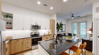 Located at 3035 North Tryon Street in Charlotte, NC, this well-appointed one-bedroom, one-bathroom residence offers a thoughtfully designed single-floor layout with modern finishes throughout. Light wood flooring flows seamlessly across the living areas, complementing the clean white walls and recessed lighting that keep the space bright and airy.

The open-concept kitchen is a standout feature, showcasing dark granite countertops, a central island with bar seating, a dual-tone cabinetry scheme combining crisp white uppers with warm wood lowers, and a full suite of stainless steel appliances. A built-in bench and open shelving near the entry provide a practical and stylish drop zone.

The living room benefits from natural light streaming through large glass French doors that open to an outdoor balcony, creating a seamless indoor-outdoor connection. A dedicated office provides a quiet, focused workspace with its own distinct area separate from the main living spaces.

The primary bedroom is comfortably proportioned, with windows that invite natural light and connect to an adjoining walk-in closet equipped with organized shelving and a stacked in-unit washer and dryer. The bathroom features a wood-toned vanity with granite countertops, a framed mirror, stylish hardware, and a soaking tub with tile surround.