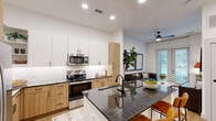 Located at 3035 North Tryon Street in Charlotte, NC, this well-appointed one-bedroom, one-bathroom residence offers a thoughtfully designed single-floor layout with modern finishes throughout. Light wood flooring flows seamlessly across the living areas, complementing the clean white walls and recessed lighting that keep the space bright and airy.

The open-concept kitchen is a standout feature, showcasing dark granite countertops, a central island with bar seating, a dual-tone cabinetry scheme combining crisp white uppers with warm wood lowers, and a full suite of stainless steel appliances. A built-in bench and open shelving near the entry provide a practical and stylish drop zone.

The living room benefits from natural light streaming through large glass French doors that open to an outdoor balcony, creating a seamless indoor-outdoor connection. A dedicated office provides a quiet, focused workspace with its own distinct area separate from the main living spaces.

The primary bedroom is comfortably proportioned, with windows that invite natural light and connect to an adjoining walk-in closet equipped with organized shelving and a stacked in-unit washer and dryer. The bathroom features a wood-toned vanity with granite countertops, a framed mirror, stylish hardware, and a soaking tub with tile surround.