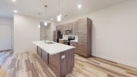 This two-story home presents a clean, modern aesthetic with a cohesive design language carried throughout both levels. The main floor centers around a well-appointed kitchen featuring wood-toned cabinetry that extends to the ceiling, offering generous storage. A large center island with a white countertop and undermount sink serves as the kitchen's focal point, illuminated by pendant lighting above. Stainless steel appliances, including a refrigerator, electric range, and built-in microwave, complete the space. Light wood-look flooring flows seamlessly across the main level, contributing to a bright, open atmosphere.

A carpeted staircase with a clean white railing leads to the upper floor, where multiple bedrooms are finished with plush carpet and ceiling fans. Each bedroom benefits from natural light provided by roller-shaded windows. The bathrooms are thoughtfully designed: a compact main-floor powder room features a pedestal sink and clean white finishes, while upper-level bathrooms offer a sliding glass-door shower stall and a separate full bath with a tub-shower combination and a vanity with contemporary hardware.