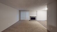 This single-floor unit located in Federal Way, Washington offers a practical and straightforward layout connecting living, sleeping, and functional spaces. The living room serves as the central gathering area, featuring wall-to-wall carpet, a textured ceiling, and a notable stone-surround fireplace as a focal point. Vertical blinds cover a sliding door, allowing natural light to filter into the space. A carpeted hallway connects the living area to the private rooms, with multiple doors leading to bedrooms and additional spaces along the way. The bedrooms are carpeted and feature textured ceilings, with windows fitted with horizontal blinds that provide natural light and privacy. The bathroom has been updated with wood-look hard-surface flooring, a white vanity with ample cabinetry, a tub-shower combination, and a window that introduces natural light. The kitchen is efficiently designed with white cabinetry, light countertops, a stainless steel sink, a white electric range, and hard-surface flooring. Track lighting overhead provides functional illumination. The overall interior maintains a neutral, clean palette throughout, with consistent finishes that create a cohesive and move-in-ready environment.