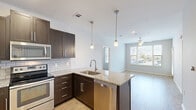 Located at 8201 Quivira Rd in Lenexa, Kansas, this two-bedroom, one-bathroom unit offers a well-designed single-floor layout that maximizes every square foot. The kitchen serves as a standout feature, showcasing dark espresso cabinetry, granite countertops, a subway tile backsplash, and a full suite of stainless steel appliances including a refrigerator, range, microwave, and dishwasher. A peninsula with pendant lighting above opens the kitchen toward the living area, which features light wood-style flooring that adds warmth throughout the common spaces. The primary bedroom is generously sized, offering a ceiling fan, a closet, and easy access to the rest of the unit. The second bedroom also includes a ceiling fan and a window that brings in natural light. Both bedrooms are finished with neutral-toned carpet, creating a comfortable feel underfoot. The bathroom is clean and functional, featuring a walk-in shower with built-in shelving and a curved curtain rod. Neutral gray walls throughout the unit provide a modern, move-in-ready aesthetic. The layout flows intuitively from the open kitchen and living area into the private sleeping quarters, making this a practical and attractive home in Lenexa, KS.