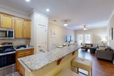 Located at 1198 Pleasant Ridge Rd in Greensboro, NC, this single-story, one-bedroom, one-bathroom home offers a thoughtfully designed layout that maximizes every square foot. The open-concept kitchen and living area serves as the heart of the home, where warm honey-toned cabinetry and granite countertops complement a stainless steel appliance suite. A peninsula with bar seating bridges the kitchen and dining area, creating an ideal space for casual meals or entertaining. Rich hardwood flooring flows throughout the main living areas, grounding the neutral, warm-toned walls.

The living room features crown molding, a ceiling fan, and a set of French doors that invite natural light and provide outdoor access, enhancing the open and airy feel of the space. The bedroom is generously sized, finished with soft carpeting and a ceiling fan, and connects directly to a spacious walk-in closet with wire shelving for ample storage. The full bathroom features hardwood floors, a shower-tub combination, and grab bars for added accessibility. A dedicated in-unit laundry room with a full-size washer and dryer adds everyday convenience. A hallway ties all rooms together for a functional, cohesive flow throughout the home.