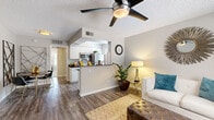 This single-floor residence offers a thoughtfully designed layout that balances comfort and functionality. The open-concept living area welcomes you with wood-look plank flooring, neutral gray walls, and a ceiling fan overhead. Large windows allow natural light to fill the space, complemented by tasteful décor that creates a warm, inviting ambiance. The living room flows seamlessly into the kitchen, which is separated by a peninsula-style breakfast bar. The kitchen is well-equipped with stainless steel appliances, including a range, microwave, refrigerator, and dishwasher, all set against crisp white cabinetry and dark granite-style countertops. A window above the counter adds natural light to the cooking space. The bedroom is a comfortable retreat, featuring plush carpeting, a ceiling fan, and a generously sized window that brings in natural light. The room offers ample space for full bedroom furnishings. The bathroom features an extended vanity topped with dark granite countertops, white cabinetry, and a wide mirror framed by bright lighting — providing both style and practicality. Throughout the residence, the consistent use of neutral tones, modern fixtures, and quality finishes creates a cohesive and polished living environment.