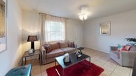 This single-story space offers a well-organized layout that balances comfort and functionality across its key living areas. The living room serves as the central gathering space, featuring light tile flooring, a ceiling fan light fixture, and a window dressed with sheer curtains that invite natural light. The room comfortably accommodates a sofa, coffee table, and entertainment setup, creating a welcoming atmosphere with a warm, neutral palette.

The kitchen is equipped with warm-toned wood cabinetry, white appliances including an electric range and dishwasher, and a double sink set beneath a window with exterior views. A separate exterior door in the kitchen adds convenient access. Light tile flooring continues throughout, maintaining visual consistency.

The two bedrooms are carpeted and naturally lit through windows with sheer drapery. Each room is generously proportioned and includes closet access. One bedroom features a ceiling fan, while both offer a calm, restful ambiance with neutral wall tones.

The bathroom includes a tub-shower combination with a curtain enclosure, toilet, and tile flooring. Its compact, efficient design serves the layout well. Overall, the space presents a clean, functional interior with consistent finishes and ample natural light throughout.