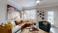 This thoughtfully designed one-bedroom, one-bathroom residence offers a cohesive single-floor layout that maximizes every inch of its compact footprint. Light wood-look flooring flows continuously throughout, unifying each space with a clean, modern aesthetic.

The open-concept living area is warm and inviting, featuring crown molding, a ceiling fan, and a large window that fills the room with natural light. The living room connects seamlessly to a defined dining nook, which includes crown molding and wall-mounted decorative shelving with greenery accents.

The galley-style kitchen is well-equipped with white shaker cabinetry, white quartz countertops, stainless steel appliances — including a range, refrigerator, and dishwasher — and a deep single-basin sink. Cabinet space extends to the ceiling, offering generous storage.

The bedroom is a calm, neutral retreat with a walk-in closet, a window with sheer curtains, and access to the bathroom via a hallway. The bathroom features a white vanity with ample drawer storage, a white countertop, and a mirrored vanity area.

Throughout the residence, neutral warm-gray walls provide a versatile backdrop, and the consistent use of light flooring enhances the sense of openness across all rooms.
