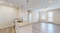 Located at 3061 Godwin Boulevard in Suffolk, Virginia, this single-floor residence offers a thoughtfully designed open-concept layout with modern finishes throughout. The kitchen serves as a central highlight, featuring white shaker-style cabinetry, granite countertops, a peninsula island with pendant lighting overhead, a stainless steel sink, and a full suite of stainless steel appliances including a refrigerator, range, microwave, and dishwasher. Recessed lighting and light wood-look flooring extend across the kitchen and into the living area, which is brightened by natural light from a large window and a sliding glass door that leads to an exterior exit. A ceiling fan adds comfort to the living space. The bedrooms are finished with plush carpeting, ceiling fans, and windows with blinds. The primary bathroom offers a double-sink granite vanity with white cabinetry, a glass-enclosed shower, and wood-look flooring, while a secondary bathroom includes a granite vanity and a tub-shower combination. The neutral warm-toned walls, clean white trim, and consistent use of quality materials throughout give the space a cohesive, contemporary feel.