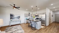 Located in Rogers, Arkansas, this two-story, 2-bedroom, 3-bathroom home offers a thoughtfully designed layout spread across two floors. The main level hosts an open-concept kitchen and living area finished with warm hardwood-style flooring. The kitchen is a standout, featuring gray shaker-style cabinetry, dark granite countertops, stainless steel appliances, and a center island with seating for two, illuminated by elegant pendant lighting. A ceiling fan completes the living space, which is bathed in natural light from large windows. A convenient bathroom is also found on this level. Upstairs, the spacious primary bedroom features plush carpet, generous natural light from oversized windows with sheer drapes, a ceiling fan, and access to a dedicated walk-in closet with full shelving and hanging rods. The primary en-suite bathroom impresses with a dual-sink vanity, dark granite countertops, gray cabinetry, and well-lit mirrors. A second bedroom is equally well-sized and carpeted, also accompanied by its own walk-in closet. A third full bathroom serves the upper floor. Throughout, the home maintains a clean, contemporary aesthetic with a neutral color palette, recessed lighting, and consistent high-quality finishes.