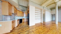 Located in the heart of downtown Rochester at 80 St Paul Street, this urban loft-style residence blends industrial character with practical living. Rich hardwood floors run throughout the space, complementing the striking exposed brick walls that lend an authentic, historic charm. Soaring ceilings with visible structural beams add to the open, airy atmosphere found throughout.

The combined kitchen and living area serves as the heart of the home, featuring warm wood cabinetry, a tile backsplash, full appliances including a dishwasher and refrigerator, and an adjacent built-in shelving unit for added storage and display. A wall of tall, multi-pane windows floods the living and dining areas with abundant natural light while offering panoramic views of the Rochester skyline.

The spacious primary bedroom continues the loft aesthetic with generous windows and the same warm hardwood floors. Three full bathrooms provide ample convenience, with finishes including stone tile and pedestal sinks. Additional highlights include four closets, two laundry areas, and a private balcony — ideal for enjoying outdoor views of the surrounding cityscape. The entry hallway is well-organized with multiple closet options. This distinctive downtown residence offers a compelling combination of historic architectural detail and urban convenience.
