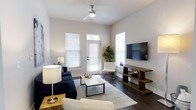 Located at 105 Ivy Green Way in Charleston, South Carolina, this single-story home offers a clean, modern aesthetic with thoughtfully designed living spaces. The living room serves as the heart of the home, showcasing rich dark hardwood flooring that runs throughout and creates a warm, grounding contrast to the crisp white walls. Elevated ceilings add a sense of openness and airiness, while a ceiling fan ensures year-round comfort. Multiple windows dressed with classic white blinds flood the space with natural light, creating a bright and welcoming atmosphere. A glass-paneled exterior door provides direct access to the outdoors, further enhancing the connection between interior and exterior. The living area is well-proportioned, offering ample room for seating arrangements and entertaining. Neutral tones throughout the interior provide a versatile backdrop that suits a variety of design preferences. The overall ambiance is contemporary yet comfortable, reflecting the relaxed charm characteristic of Charleston living. This home combines practical single-floor convenience with stylish finishes, making it an inviting and functional residence in a well-established community.