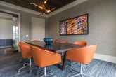 Located at 903 Huff Rd NW in Atlanta's vibrant West Midtown corridor, this single-floor conference space blends industrial heritage with refined modern design. The room's most striking architectural feature is its exposed red brick walls, accented by sweeping arched openings that frame large, steel-framed windows. These expansive windows flood the interior with natural light while offering open views into an adjacent atrium and the surrounding neighborhood beyond.

The ceiling is clad in warm, dark-stained wood planks, creating a rich contrast against the textured brick and crisp white crown molding that lines the room's perimeter. Recessed lighting and a sculptural pendant fixture provide layered illumination throughout. Underfoot, a patterned commercial carpet in deep blue-gray tones adds depth and a polished, professional feel.

At the center of the room sits a substantial dark conference table surrounded by curved, cognac-leather chairs, offering both comfort and style for meetings and collaborative sessions. The walls are finished in a refined gray fabric-textured treatment, providing a calm, neutral backdrop accented by a bold urban cityscape artwork that adds a vibrant, local character to the space. An adjacent private office with its own brick detailing and natural light is accessible directly from the conference room, extending the functionality of the overall suite.