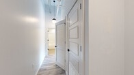 This single-floor unit showcases a thoughtfully designed open-concept layout that blends modern finishes with industrial character. Soaring ceilings with exposed ductwork and structural elements lend an urban loft aesthetic throughout, while globe pendant lighting adds warm, stylish illumination to the main living areas.

The kitchen is a standout feature, outfitted with crisp white shaker-style cabinetry, light granite countertops, and a classic white subway tile backsplash. A full suite of stainless steel appliances — including a refrigerator, electric range, over-the-range microwave, and dishwasher — provides everything needed for everyday living.

Light wood-look luxury vinyl flooring runs consistently throughout the unit, creating a cohesive and easy-to-maintain aesthetic. The open living area is generously proportioned, offering flexible arrangements and benefiting from large windows that draw in natural light.

The bathroom is cleanly appointed with a white vanity, tub-shower combination with tiled surround, and coordinating flooring. A hallway fitted with louvered and paneled doors provides practical storage access, keeping the living areas uncluttered. Black hardware accents appear consistently throughout, from door handles to hinges, tying together the modern design language. Overall, this unit delivers a fresh, contemporary living environment with industrial-inspired touches.