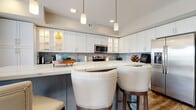 Located at 400 N Main St in Royal Oak, MI, this single-floor residence offers a thoughtfully designed layout with modern finishes throughout. The open-concept kitchen is a standout feature, showcasing white shaker-style cabinetry with glass-front accents, quartz countertops, a farmhouse sink, stainless steel appliances, and a striking hexagonal tile backsplash. A gray island with seating provides additional workspace and casual dining. Rich hardwood-style flooring flows through the main living areas, connecting the kitchen to a bright living room complete with a wall-mounted entertainment center and large windows that invite natural light.

The bedrooms offer a calm, neutral aesthetic with plush carpeting, tufted upholstered headboards, and windows with outdoor views. The bathrooms feature large-format tile flooring, a dark wood vanity with quartz countertop, and a combination tub and shower with chrome fixtures. A dedicated laundry room adds practicality, equipped with a side-by-side washer and dryer beneath an expansive quartz folding surface and ample upper cabinetry. The overall ambiance is clean, contemporary, and well-organized, reflecting a high standard of modern residential design.