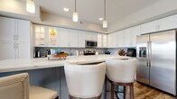 Located at 400 N Main St in Royal Oak, MI, this single-floor residence offers a thoughtfully designed layout with modern finishes throughout. The open-concept kitchen is a standout feature, showcasing white shaker-style cabinetry with glass-front accents, quartz countertops, a farmhouse sink, stainless steel appliances, and a striking hexagonal tile backsplash. A gray island with seating provides additional workspace and casual dining. Rich hardwood-style flooring flows through the main living areas, connecting the kitchen to a bright living room complete with a wall-mounted entertainment center and large windows that invite natural light.

The bedrooms offer a calm, neutral aesthetic with plush carpeting, tufted upholstered headboards, and windows with outdoor views. The bathrooms feature large-format tile flooring, a dark wood vanity with quartz countertop, and a combination tub and shower with chrome fixtures. A dedicated laundry room adds practicality, equipped with a side-by-side washer and dryer beneath an expansive quartz folding surface and ample upper cabinetry. The overall ambiance is clean, contemporary, and well-organized, reflecting a high standard of modern residential design.