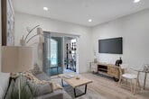 Located at 7199 Citrus Ave in Fontana, California, this thoughtfully designed single-story residence offers a clean, contemporary aesthetic throughout. Light wood-tone flooring flows seamlessly across the entire space, creating a cohesive and airy feel from room to room.

The open-concept living area connects directly to the kitchen, maximizing the sense of space. The kitchen is outfitted with stainless steel appliances — including a full-size refrigerator, range, and microwave — complemented by light wood cabinetry, a white tile backsplash, and ample counter space. Recessed lighting illuminates the area efficiently.

The living room provides a comfortable, well-lit retreat, featuring a sliding glass door that opens to a private outdoor patio, allowing for natural light and easy indoor-outdoor access. Crisp white walls throughout the home serve as a neutral backdrop that enhances the bright, open atmosphere.

The bedroom is generously proportioned, with a window that invites natural light and a layout accommodating a full dresser and wall-mounted television. The bathroom is finished with modern fixtures, a light wood vanity, and a glass-enclosed tub and shower combination adorned with elegant marble-style tile surround. Every detail reflects a commitment to clean, functional, and stylish living.