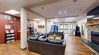 Located at 111 Honeysuckle Lane in Bloomsburg, PA, this expansive single-floor amenity center serves as the community hub for Honeysuckle Student Apartments. The space is thoughtfully designed to support student living with a wide range of shared facilities.

The welcoming main lounge greets visitors with warm hardwood-style flooring, comfortable leather seating, a striking stone fireplace, and glass entry doors that allow abundant natural light to fill the space. Vending machines and open sightlines to the outdoors add to the relaxed, communal atmosphere.

The expansive fitness center is divided into two well-equipped zones: a cardio area featuring treadmills, ellipticals, and stair climbers set against vibrant teal walls, and a strength training area outfitted with weight machines and benches accented by bold blue walls with motivational signage.

A dedicated computer lab offers multiple workstations along wood-topped desks, a multifunction printer, and soft yellow walls that create a focused study environment. An adjoining conference room provides a professional setting with an oval table, leather chairs, a wall-mounted TV, and a chalkboard — ideal for group meetings or study sessions.

The kitchen features warm wood cabinetry, a decorative tile backsplash, a full sink, microwave, and dishwasher. Hallways connect all areas efficiently, completing a well-rounded amenity space designed for student convenience and community.