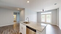 Located on Founder's Lane in Lebanon, Ohio, this well-appointed single-story home offers three bedrooms, two bathrooms, and a thoughtfully designed layout. The open-concept kitchen and living area serves as the heart of the home, featuring rich hardwood-style flooring, a ceiling fan, and French doors with transom windows that flood the space with natural light and provide outdoor views. The kitchen is a standout, boasting granite countertops, a large center island with an undermount sink, crisp white shaker cabinetry, and a full suite of stainless steel appliances including a range, microwave, and refrigerator. The bedrooms are carpeted for comfort, with the secondary bedrooms offering generous proportions, natural light from exterior windows, and sliding double-door closets. The primary bedroom includes a spacious walk-in closet fitted with wire shelving and hanging rods. The two bathrooms are finished with granite-topped vanities and wood-style flooring — one featuring a tub-shower combo, the other a standalone walk-in shower with brushed nickel fixtures. A dedicated laundry room with washer and dryer hookups adds everyday convenience. Neutral gray tones throughout lend the home a clean, contemporary feel.