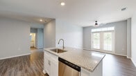Located on Founder's Lane in Lebanon, Ohio, this well-appointed single-story home offers three bedrooms, two bathrooms, and a thoughtfully designed layout. The open-concept kitchen and living area serves as the heart of the home, featuring rich hardwood-style flooring, a ceiling fan, and French doors with transom windows that flood the space with natural light and provide outdoor views. The kitchen is a standout, boasting granite countertops, a large center island with an undermount sink, crisp white shaker cabinetry, and a full suite of stainless steel appliances including a range, microwave, and refrigerator. The bedrooms are carpeted for comfort, with the secondary bedrooms offering generous proportions, natural light from exterior windows, and sliding double-door closets. The primary bedroom includes a spacious walk-in closet fitted with wire shelving and hanging rods. The two bathrooms are finished with granite-topped vanities and wood-style flooring — one featuring a tub-shower combo, the other a standalone walk-in shower with brushed nickel fixtures. A dedicated laundry room with washer and dryer hookups adds everyday convenience. Neutral gray tones throughout lend the home a clean, contemporary feel.