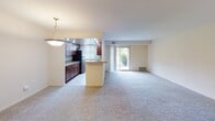 This single-floor residence at Veterans Highway in Levittown, Pennsylvania offers a well-organized layout with a clear separation between living, sleeping, and bathroom areas. The galley-style kitchen is a standout feature, finished with rich dark wood cabinetry lining both walls, granite-style countertops, recessed lighting, and stainless steel appliances including a gas range, microwave, dishwasher, and refrigerator. A peninsula with pendant lighting connects the kitchen to the open living and dining area, which is carpeted and benefits from natural light through a sliding glass door that opens to an outdoor view. The spacious living area provides a comfortable, open atmosphere suitable for a variety of furniture arrangements. The bedrooms are carpeted and feature neutral walls with windows admitting natural light; one bedroom offers an exterior view of greenery. The bathrooms are functional and clean in design: one includes a tiled tub-shower combination with a curved curtain rod, a white vanity with sink, and tile flooring, while a second bathroom features a walk-in shower enclosed by glass doors with tile surround. Overall, the unit presents a clean, neutral palette throughout.