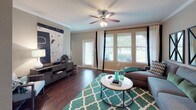 This 2-bedroom, 2-bathroom single-story residence offers a thoughtfully designed layout that balances comfort and functionality. The living area is a welcoming space featuring rich hardwood flooring, crown molding, and a ceiling fan with light fixture. Large windows allow abundant natural light to fill the room, while a sliding glass door provides access to the outdoors and views of the surrounding greenery.

The kitchen is equipped with warm wood cabinetry, a double stainless steel sink, white appliances including a range and built-in microwave, and ample counter space. Crown molding adds an elegant touch, and under-cabinet lighting enhances the workspace.

Both bedrooms are generously sized with plush carpeting, crown molding, and ceiling fans. Each features a walk-in closet, providing excellent storage. The primary bedroom connects to a private en-suite bathroom complete with a soaking tub, tiled surround, a wood vanity, and a large mirror. The second bathroom features a glass-enclosed walk-in shower, a wood vanity with a single sink, and tile flooring. The overall ambiance throughout the residence is warm, neutral, and inviting.