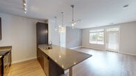 This contemporary single-floor residence offers a thoughtfully designed open-concept layout that seamlessly connects the kitchen, dining, and living areas. The kitchen is a standout feature, showcasing rich dark-wood cabinetry, a large granite-topped island with an integrated sink, and elegant pendant lighting suspended above. Stainless steel appliances, including a French door refrigerator, electric range, and built-in microwave, complete the well-appointed culinary space. Light hardwood flooring flows throughout the main living areas, enhancing the bright, airy atmosphere. The spacious living area benefits from generous natural light streaming through large windows and a glass door that opens to an outdoor balcony. The primary bathroom is equipped with a dual-sink vanity featuring dark wood cabinetry, stone countertops, a large mirror, and a walk-in glass-enclosed shower. A secondary bathroom offers a combination tub and shower alongside a matching single-sink vanity. The bedrooms are comfortably sized and carpeted, each with windows that allow natural light to fill the rooms. Track lighting and recessed fixtures throughout the unit provide functional and ambient illumination, contributing to a clean, modern aesthetic across the entire space.