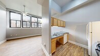 Located at 166 W Broadway St in Winona, Minnesota, this one-bedroom, one-bathroom unit offers a functional and well-organized layout across a single floor. The open-concept design connects the kitchen and living area, creating a cohesive and airy feel enhanced by notably high ceilings throughout. The kitchen features warm honey-toned cabinetry, gray laminate countertops, a double-basin sink, and white appliances including a refrigerator and electric range. A pass-through window opens the kitchen toward the living space, improving sightlines and natural light flow. The living room benefits from large black-framed windows that invite abundant natural light and views of the surrounding streetscape, and is equipped with a ceiling fan. The bedroom is carpeted, comfortably sized, and includes black-framed windows that mirror the living area's aesthetic. Three closets throughout the unit provide generous storage options. The bathroom is designed with accessibility in mind, featuring grab bars, a roll-in shower area, and easy-clean flooring. A dedicated utility room rounds out the unit's practical offerings. Hardwood-style flooring runs through the main living and kitchen areas, complementing the clean, neutral color palette found throughout the space.