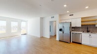 Located at 22520 Lyons Ave in Santa Clarita, CA, this single-floor residence offers a clean, modern aesthetic throughout. The open-concept living and kitchen area is anchored by warm light wood flooring, recessed lighting, and crisp white walls that create a bright, welcoming atmosphere. A sliding door provides access to an outdoor area and allows natural light to flow into the living space.

The kitchen is well-appointed with white shaker-style cabinetry, light quartz countertops, and a gray subway tile backsplash. Stainless steel appliances — including a French door refrigerator with ice maker, dishwasher, electric range, and over-the-range microwave — complete the functional and stylish cooking space. A wood-accented open shelf adds a warm design detail.

The bedrooms feature plush carpeting and large windows that bring in abundant natural light, offering a comfortable and airy feel. Two full bathrooms serve the unit, each finished with light wood-tone flooring, white subway tile tub surrounds, white vanities with quartz countertops, and modern LED-backlit mirrors, lending a clean and contemporary look. The consistent use of neutral tones and modern finishes throughout the space creates a cohesive, move-in-ready environment.