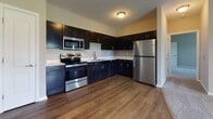 Located at 2003 Persimmon Way in Huber Heights, Ohio, this single-story home offers a well-organized layout with a cohesive, modern design throughout. The kitchen serves as a functional centerpiece, outfitted with dark espresso cabinetry extending to the upper walls, light countertops, and a full suite of stainless steel appliances including a range, microwave, dishwasher, and refrigerator. Wood-look plank flooring runs through the kitchen and main living areas, lending warmth and continuity to the space.

The living area transitions smoothly from the kitchen, with neutral gray walls and an entry corridor providing clear sightlines through the home. Bedrooms are carpeted and feature ceiling fans, neutral tones, and windows that allow natural light. Closets with built-in shelving and panel doors offer practical storage. One bathroom includes a full tub-shower combination with white tile surround and wood-look flooring, while a second bathroom provides a more compact layout. A dedicated laundry area accommodates a full-size washer and dryer with overhead wire shelving. The overall aesthetic is clean, neutral, and move-in ready.
