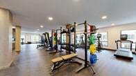 Located in Woodinville, Washington, this well-appointed fitness center offers a generously sized, single-floor exercise space designed to accommodate a wide range of workout needs. The open floor plan is anchored by structural columns finished in warm wood tones, lending the space a modern, clean aesthetic that complements the neutral-toned carpeted flooring throughout.

The cardio zone features a row of elliptical trainers and treadmills positioned along the windowed perimeter, allowing natural light to fill the space and providing views of the surrounding greenery. The strength training area is equipped with multiple cable machines, multi-functional racks loaded with weight plates and medicine balls, adjustable benches, and an extensive dumbbell rack with a full mirror behind it for form monitoring.

A dedicated functional training section offers open floor space for free movement and stretching. Built-in wooden shelving units provide organized storage for accessories such as towels and fitness equipment. Recessed ceiling lighting ensures even, bright illumination throughout the entire facility.

The space also includes a tiled accent column serving as an architectural focal point, glass-panel room dividers, and wall-mounted displays. Large windows along multiple walls draw in natural light and connect the interior to the outdoor environment, creating an inviting and energizing atmosphere for workouts.